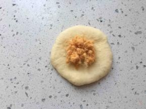 取一个松弛好的面团，按扁，拍掉周围气泡，边缘压薄些，包入适量肉松