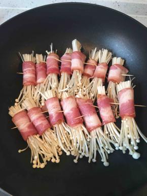 不沾平底锅预热，放入金针菇卷。不需要放油，培根在煎的过程中会出油