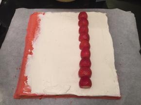 蛋糕片出炉后盖上油纸，倒扣放至微热，淡奶油加糖打发至六七成，抺在蛋糕正面，放上洗净擦干的草莓