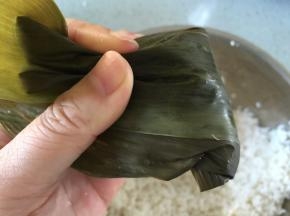 装满米后，把糯米稍微捏扁一点，把粽叶向下折，把米包住，形成四个尖角