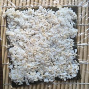 取一张紫菜放在寿司帘上。
米饭用少许白糖和寿司醋拌匀后平铺在紫菜上。