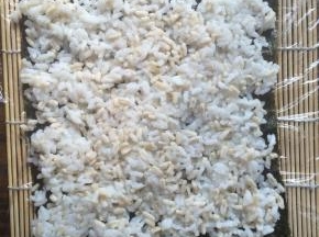 取一张紫菜放在寿司帘上。
米饭用少许白糖和寿司醋拌匀后平铺在紫菜上。