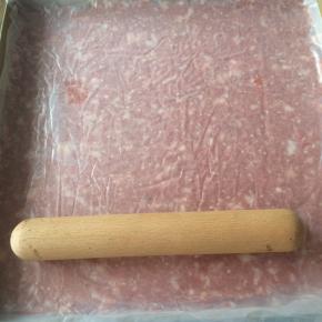 猪肉糜上垫一张保鲜膜，借助擀面杖将肉糜擀成薄厚均匀的片状。