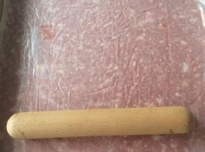 猪肉糜上垫一张保鲜膜，借助擀面杖将肉糜擀成薄厚均匀的片状。