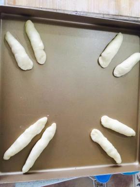 把8个小面团搓成10cm长的橄榄形，做兔子的耳朵，做好的耳朵放在烤盘上，用手一端按扁