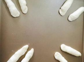 把8个小面团搓成10cm长的橄榄形，做兔子的耳朵，做好的耳朵放在烤盘上，用手一端按扁