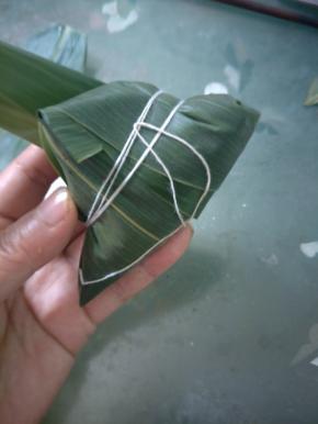 用粽叶盖住馅料，向前翻。
顺着粽子的尖角翻折，剩余的粽叶顺着粽子的形状包裹即可。绕着粽子多缠几圈，缠紧一点防止粽叶散开。