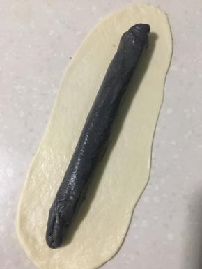 在用白色面皮完全包裹黑色长条，长条两头要收紧封好。