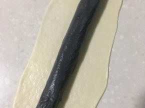 在用白色面皮完全包裹黑色长条，长条两头要收紧封好。