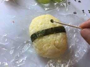 海苔剪一条长方形，在饭团中心偏下位置包起来。用牙签将眼睛粘到合适的位置。