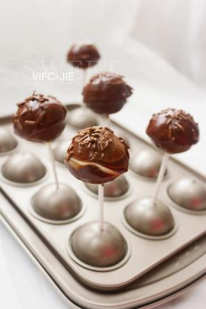 黑巧克力隔水溶化，把刚刚沾好白巧克力的棒棒糖蛋糕再在黑巧克力上沾一次，这样成品能看出有双色巧克力，然后在表面撒上一些黑巧克力针做装饰