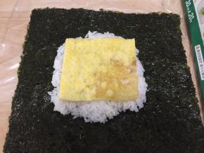 取另两张保鲜膜铺上，放入紫菜片和米饭、蛋片