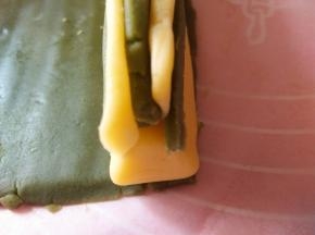 将抹茶面团切3个0.6CM宽的长条，依次叠起来放在兔兔脸的上方（垫油纸压实，防止有空间）两个耳朵分别放两侧（压实）抹茶面团再切出2个0.3CM的长条放在耳朵两侧（压实）