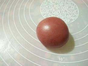 （8）将两种不同颜色的面饼叠放，中间放上椰蓉馅，右手压住内馅，左手一边转一边收口，最后把饼皮收拢，收口朝下，放置在烤盘上。