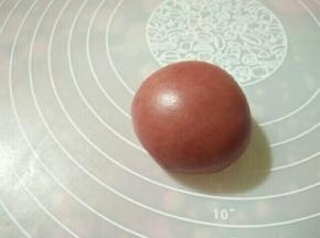 （8）将两种不同颜色的面饼叠放，中间放上椰蓉馅，右手压住内馅，左手一边转一边收口，最后把饼皮收拢，收口朝下，放置在烤盘上。