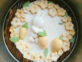 小兔子底部抹少许水固定在刚才擀好醒发的面饼上，然后在合适的位置固定好萝卜，最后在面饼周围抹少许水沾一圈大小不同的花朵，(花朵可以用筷子摁一下，沾合会更牢固，还可以有花芯的感觉)，沾几片绿叶做衬托。完成