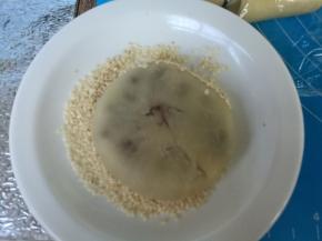 白芝麻放盘，摊平，刷蛋液，沾白芝麻，排入烤盘。