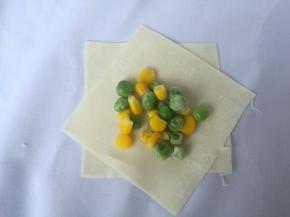 取两片馄饨皮，交叉叠放一起，放入适量青豆和玉米粒。