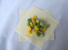 取两片馄饨皮，交叉叠放一起，放入适量青豆和玉米粒。