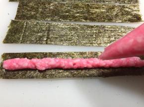 把粉色米饭放入裱花袋中，剪口，挤在海苔条的中央。