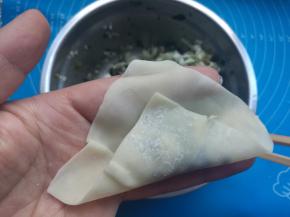 馄饨皮放左手手指之间，放入馅，对角卷起馄饨皮。