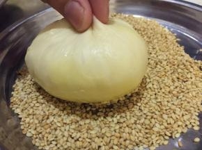 将刷蛋黄液的一面圴匀地沾上熟白芝麻