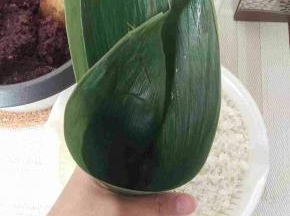 2：把粽叶2张叠在一起，靠近自己的一张放上面并且靠近自己1-2CM这样。这样可以包的比较大点，在粽子叶的中间靠左一点的地方两手抓着叶子往身体的反方向折起来，下面尾巴要留2cm左右并且向左折过来，这样不会漏。厉害的用一张就好，2张是比较安全，不容易漏。



