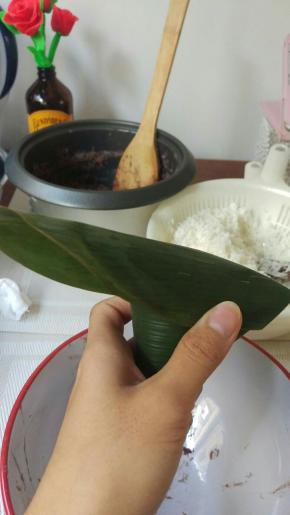 左大拇指和食指手抓粽子的2边，右手把上面多于的粽叶盖上去，边缘2边盖上去后往下折。上面多于的位置，往中间捏紧后折向身体的方向。




