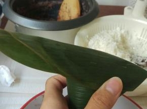 左大拇指和食指手抓粽子的2边，右手把上面多于的粽叶盖上去，边缘2边盖上去后往下折。上面多于的位置，往中间捏紧后折向身体的方向。




