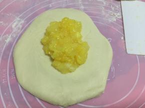 将面团排气后收紧成圆形，压扁后勺入凤梨果酱陷再收紧包住