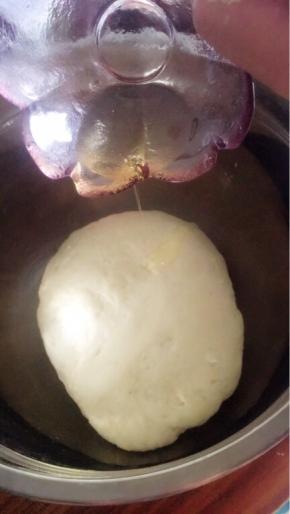 将面粉和糖倒入酵母水中，用筷子搅拌一下，开始揉面，揉至“三光”，倒入油，接着揉。