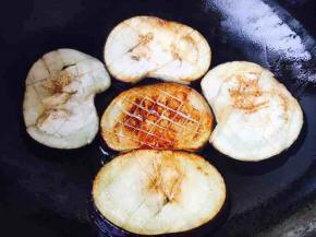 当一面煎至金黄色时翻过来再煎另一面。由于锅受热不均匀，要随时查看每一片茄子的状态，如锅里中间的那片这面就是煎好的。煎茄子时一次不要放太多的油，随煎随添加油。