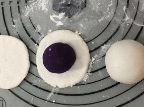 拿一个面团，用手挰成中间厚四周薄的饼，然后将紫薯球放在饼中间，用手一点点的将紫薯球包入，不要将紫薯馅露出