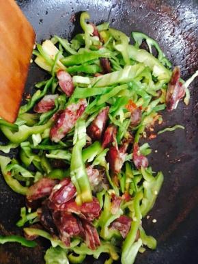 倒入腊肠和尖椒，翻炒片刻。