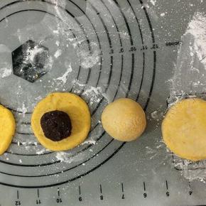 搓圆的面团，用手按成四周薄中间厚的圆饼，拿个豆馅放在饼中间，右手转圈慢慢的将面饼往上推，左手将馅轻轻的住里按，然后包好，双手将它滚圆，不要露出馅，用手心轻轻按成小圆饼坯