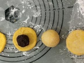 搓圆的面团，用手按成四周薄中间厚的圆饼，拿个豆馅放在饼中间，右手转圈慢慢的将面饼往上推，左手将馅轻轻的住里按，然后包好，双手将它滚圆，不要露出馅，用手心轻轻按成小圆饼坯