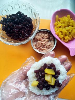 在做蜜红豆的拿一团米饭按扁放入蜜红豆和寿司萝卜，用手捏紧成圆形。