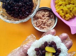 在做蜜红豆的拿一团米饭按扁放入蜜红豆和寿司萝卜，用手捏紧成圆形。