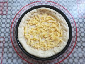 在披萨面团上抹上适量的沙拉酱，再放上适量的马苏里拉奶酪碎