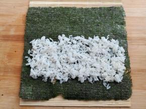 在寿司帘上放上大片的紫菜，铺上一部分的米饭，前段留一半，末端留一小节不铺米饭