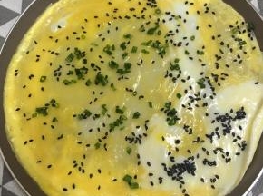 倒入蛋液，撒入葱花和黑芝麻，小火继续煎至蛋液凝固。