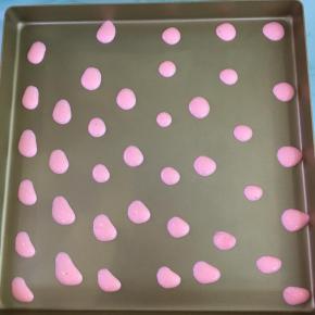 将粉色蛋糕糊在不粘烤盘上挤出小圆点。