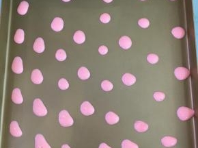 将粉色蛋糕糊在不粘烤盘上挤出小圆点。