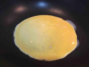 倒入一半鸡蛋液，将平底锅端起转一圈，将蛋液分布均匀。