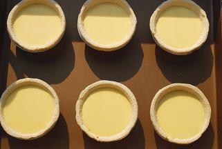 蛋挞皮取出，放金盘中，倒入挞液