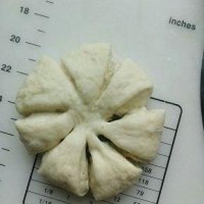 留出中心位置，用剪刀剪出8个开口；烤盘放入烤箱，同时放入一碗热水，继续进行最后发酵；最后发酵结束后，表面刷蛋液，中心撒适量芝麻点缀.