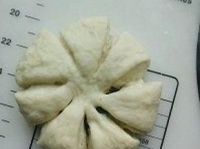 留出中心位置，用剪刀剪出8个开口；烤盘放入烤箱，同时放入一碗热水，继续进行最后发酵；最后发酵结束后，表面刷蛋液，中心撒适量芝麻点缀.