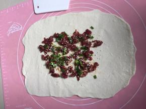 将腌制好的牛肉放入擀开的面团中央，撒上黑椒碎、白芝麻、葱花