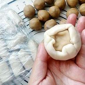 取一块面团按扁放入莲蓉玫瑰馅料，用虎口转的包紧。底部压住。