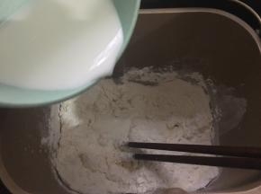 饼底材料中的高粉、低粉、盐、糖和酵母倒入面包机桶里，加入纯牛奶，用筷子搅拌成棉絮状